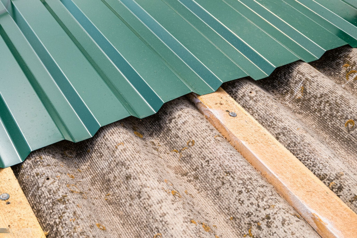 Green metal roof sheet being installed over old, weathered corrugated roofing for an eco-friendly upgrade.